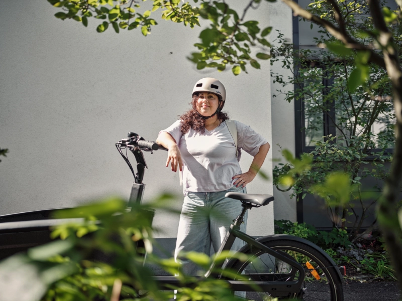 Eine Frau lehnt stolz an ihrem Lastenrad und trägt einen Helm. Eine Frau lehnt stolz an ihrem Lastenrad und trägt einen Helm.